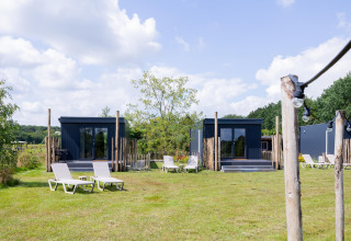 Tiny houses met terrassen en ligstoelen op het gras bij The Kremmer in Nederland op een zonnige dag.
