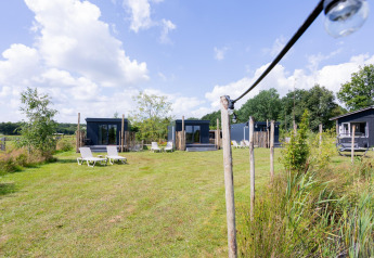 Prato verde con piccole tiny house nere e sdraio presso Tiny House con terrazza a The Kremmer, Paesi Bassi.