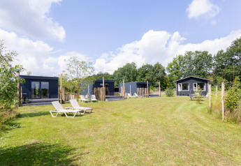 Tiny House con terraza en The Kremmer, Países Bajos, rodeada de césped y tumbonas en un entorno natural.