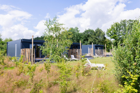 Moderne Tiny Houses mit Terrasse in grüner Umgebung bei The Kremmer, Niederlande, bei Sonnenschein.