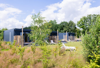 Moderne tiny houses met terras in een groene tuin bij The Kremmer, Nederland, onder blauwe hemel.