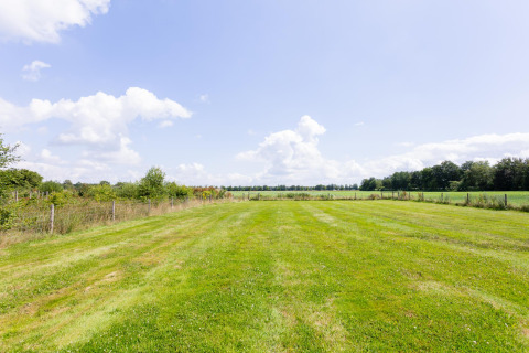 Uitzicht op een groen veld met hek en bomen bij Tiny House met terras bij The Kremmer, Nederland.