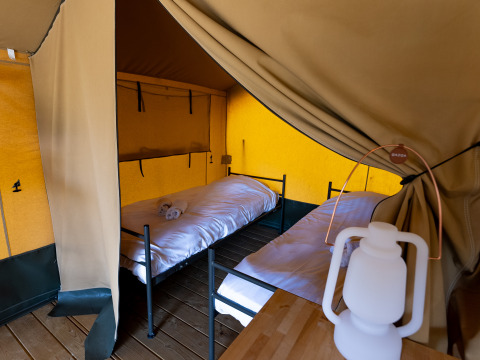 Vista interior de la tienda Safari tent Heeg en Marina Heeg, Países Bajos, con dos camas y una lámpara.