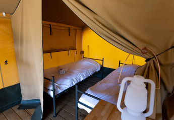 Vista interior de la tienda Safari tent Heeg en Marina Heeg, Países Bajos, con dos camas y una lámpara.