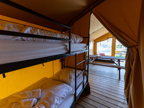 Interieur van een safaritent met stapelbedden en houten tafel bij Marina Heeg in Nederland.