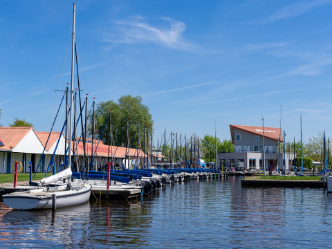 Både ved kaj i et roligt farvand med glampingindkvartering og blå himmel i baggrunden.