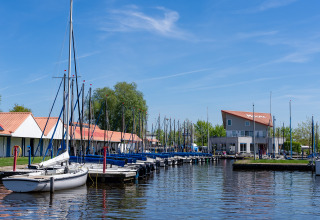 Boten aangemeerd aan een glamping-accommodatie met blauwe lucht en kalm water op de voorgrond.