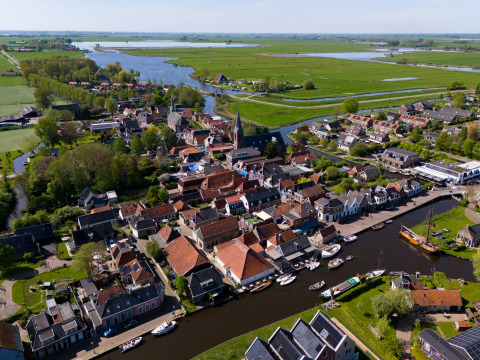 Luchtfoto van Houseboat Heeg bij Marina Heeg in Nederland, omgeven door water, boten en groene weilanden.