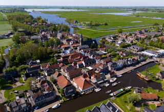 Luchtfoto van Houseboat Heeg bij Marina Heeg in Nederland, omgeven door water, boten en groene weilanden.