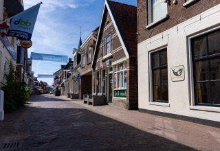 A quiet cobblestone street with small shops and banners in a Dutch town, taken at a glamping accommodation.