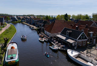 Canal con botes, casas junto al agua y terraza de café exterior en alojamiento glamping en Holanda.