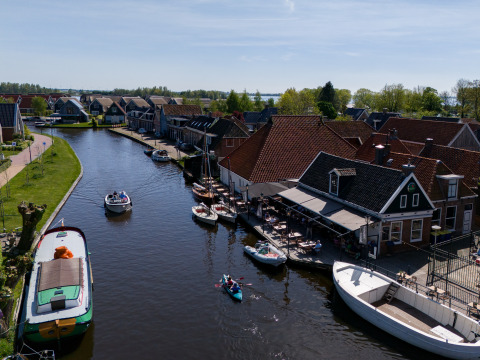 Kanaal met boten, huizen en een terras bij een glampingverblijf onder mooie blauwe hemel in Nederland.