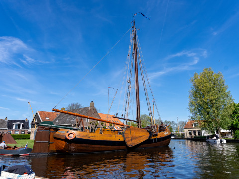Traditionelles Holzsegelboot im Hafen von Heeg, Niederlande, mit Häusern und Bäumen im Hintergrund.