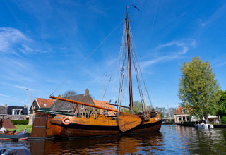 Traditionelles Holzsegelboot im Hafen von Heeg, Niederlande, mit Häusern und Bäumen im Hintergrund.