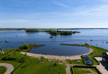 Vue sur la plage et le lac depuis Houseboat Heeg à la Marina Heeg, Pays-Bas, sous un ciel bleu clair.