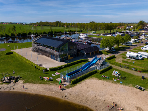 Et glampingsted med en rutsjebane, sandstrand, camperpladser og bådehavnen i baggrunden.