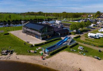 Et glampingsted med en rutsjebane, sandstrand, camperpladser og bådehavnen i baggrunden.