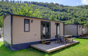 Foto von modernen Ferienhütten mit Holzterrasse und Sitzgelegenheiten, umgeben von grüner Natur und Hügeln.