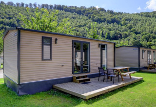 Foto van moderne blokhutten met houten terrassen en picknicktafels aan de rand van een beboste heuvel.