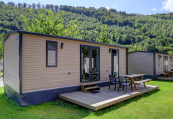 Foto van moderne blokhutten met houten terrassen en picknicktafels aan de rand van een beboste heuvel.