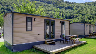 Foto van moderne chalets met houten terras en tuinmeubilair, gelegen aan de voet van groene, beboste heuvels.