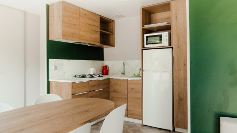 Moderne cabinakeuken met houten kasten, gaskookvuur, witte koelkast, microgolfoven en eettafel.