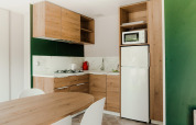 Moderne cabinakeuken met houten kasten, gaskookvuur, witte koelkast, microgolfoven en eettafel.