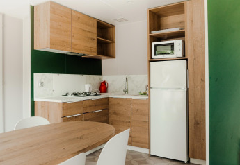Moderne cabinakeuken met houten kasten, gaskookvuur, witte koelkast, microgolfoven en eettafel.