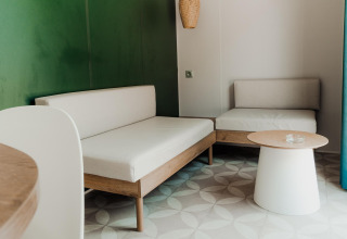 Salotto moderno in una cabina con mobili chiari, parete verde, tavolino e luce naturale.