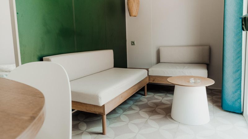 Moderne woonkamer in een hut met lichte meubels, groene muur, rond tafeltje en veel daglicht.