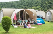 Famiglia rilassata davanti a una tenda safari Coco Sweet in campeggio, con biciclette e colline sullo sfondo.