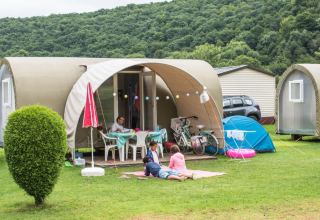 Gezin geniet voor een Coco Sweet safaritent op de camping, omringd door fietsen en groene heuvels.
