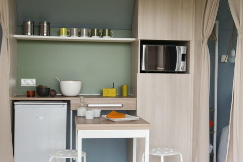 Cocina pequeña y moderna en una tienda Coco Sweet, con microondas, nevera y barra para comer.