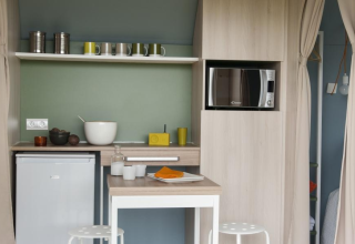 Cocina pequeña y moderna en una tienda Coco Sweet, con microondas, nevera y barra para comer.