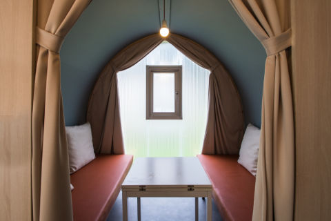Interieur van een Coco Sweet safaritent met twee banken, tafel, klein raam en beige gordijnen open.