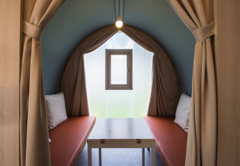 Intérieur d’une tente safari Coco Sweet avec deux banquettes, une table, une fenêtre et des rideaux beiges.
