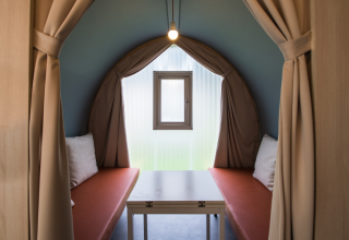 Interior de una tienda safari Coco Sweet con dos bancos, mesa, ventana pequeña y cortinas beige abiertas.