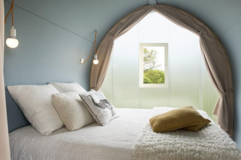 Binnen in de Coco Sweet safaritent, comfortabel bed met kussens, raam met uitzicht op groene natuur.