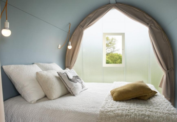 Interior de la tienda safari Coco Sweet, con cama cómoda, cojines y ventana con vista a la naturaleza.