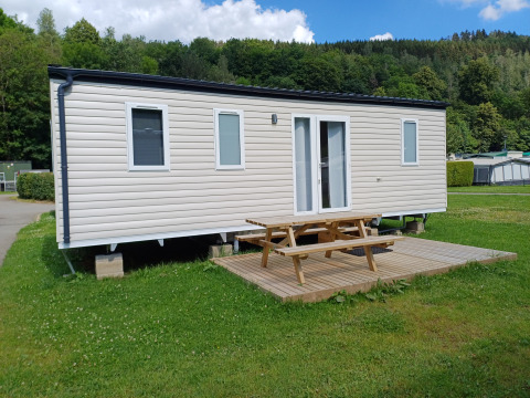 Foto di una moderna casa mobile con terrazza in legno e tavolo da picnic su un prato verde.