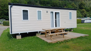 A photo of a modern cabin with a wooden deck and picnic table, set on a grassy area at a campground.