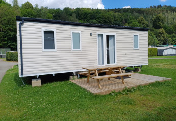 A photo of a modern cabin with a wooden deck and picnic table, set on a grassy area at a campground.