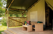 Glampingverblijf met een overdekt houten terras, gezellige zithoek en uitzicht op een groene omgeving.