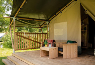 Glamping accommodation with a covered wooden deck, cozy outdoor seating, and surrounded by greenery.