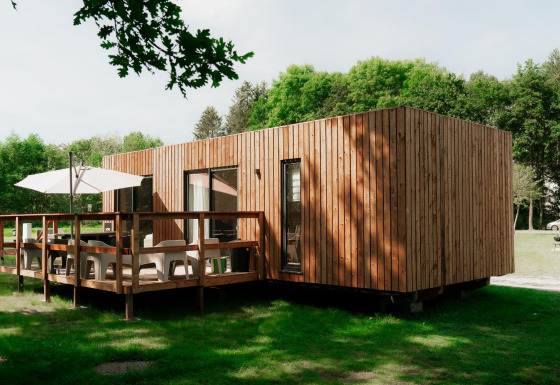 Alojamiento glamping moderno con fachada de madera y terraza, rodeado de naturaleza verde.