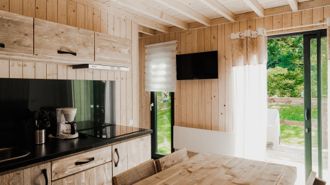 Moderne glamping accommodatie met houten keuken, eetruimte, tv en zicht op het groen buiten.