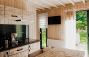 Alloggio glamping moderno con cucina in legno, tavolo da pranzo, TV e vista sulla natura esterna.