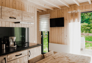 Alloggio glamping moderno con cucina in legno, tavolo da pranzo, TV e vista sulla natura esterna.