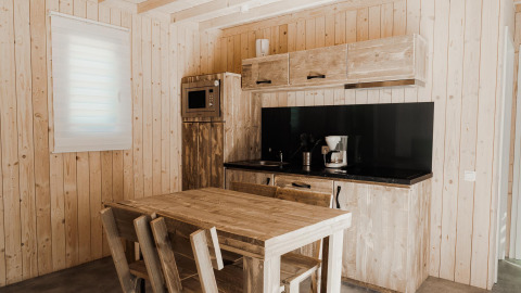 Cocina de glamping moderna con paredes de madera, mesa, cafetera, microondas y encimera negra.