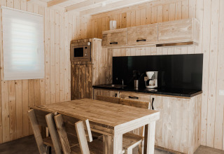 Cocina de glamping moderna con paredes de madera, mesa, cafetera, microondas y encimera negra.